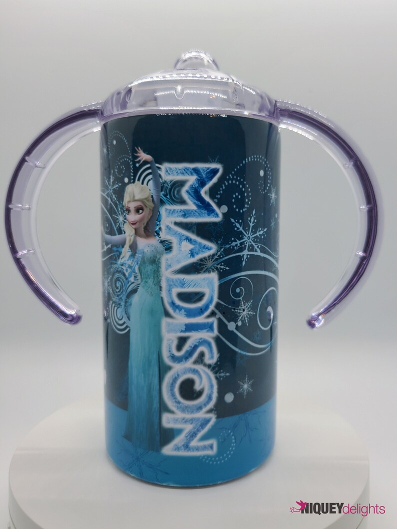 K&ouml;nnte beinhalten: Blau-wei&szlig;er Trinkbecher mit Elsa aus Frozen und dem Namen "Madison". Er hat einen transparenten Deckel, lila Griffe und einen blauen Boden. Geeignet f&uuml;r Kleinkinder.