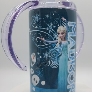 K&ouml;nnte beinhalten: Ein blau-wei&szlig;er Trinkbecher mit der Figur Elsa aus dem Film Frozen, mit dem Namen "Madison" auf der Seite. Der Becher hat transparente lila Griffe und einen Deckel und ist mit Schneeflocken und der Figur Olaf verziert.
