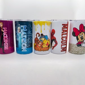 K&ouml;nnte beinhalten: F&uuml;nf personalisierte Becher mit verschiedenen Designs. Einer hat einen lila Glitzerhintergrund mit dem Namen "Mackenzie" und einem Frozen-Charakter. Ein anderer hat "Madison" und Elsa. Weitere Becher zeigen Winnie the Pooh, Spider-Man und Minnie Mouse.