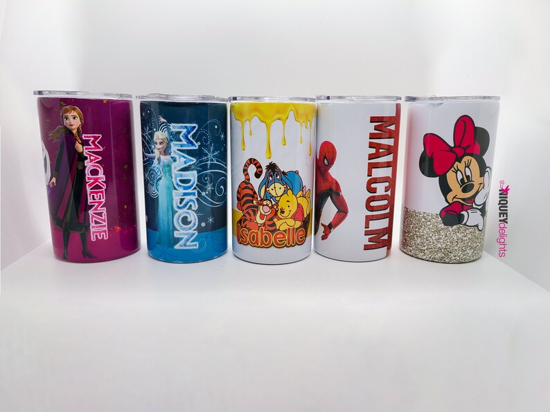 K&ouml;nnte beinhalten: F&uuml;nf personalisierte Becher mit verschiedenen Designs. Einer hat einen lila Glitzerhintergrund mit dem Namen "Mackenzie" und einem Frozen-Charakter. Ein anderer hat "Madison" und Elsa. Weitere Becher zeigen Winnie the Pooh, Spider-Man und Minnie Mouse.