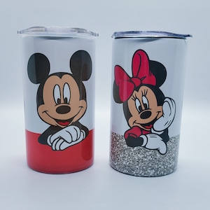 May include: Two stainless steel tumblers featuring Mickey and Minnie Mouse. One tumbler has a red base and Mickey's image, the other has a glitter base and Minnie's image. Both have clear lids.