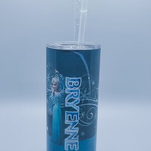 K&ouml;nnte beinhalten: Ein blauer Becher mit Deckel und einem durchsichtigen Strohhalm. Der Becher zeigt ein Design einer Figur aus dem Film Frozen, mit dem Namen "BRYENNE" in Wei&szlig;. Der Hintergrund ist ein Blauton.