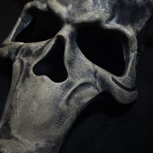 May include: A gray and black skull mask with horns. The mask has a weathered, distressed look.
