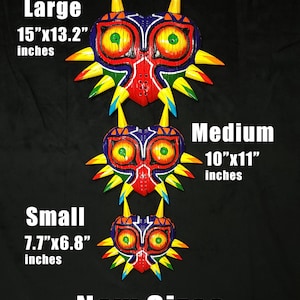 May include: Three different sizes of a Majora's Mask from The Legend of Zelda video game. The masks are made of wood and painted in bright colors, including red, yellow, green, blue, and purple. The masks are arranged from largest to smallest, with the largest mask measuring 15 inches by 13.2 inches, the medium mask measuring 10 inches by 11 inches, and the smallest mask measuring 7.7 inches by 6.8 inches.