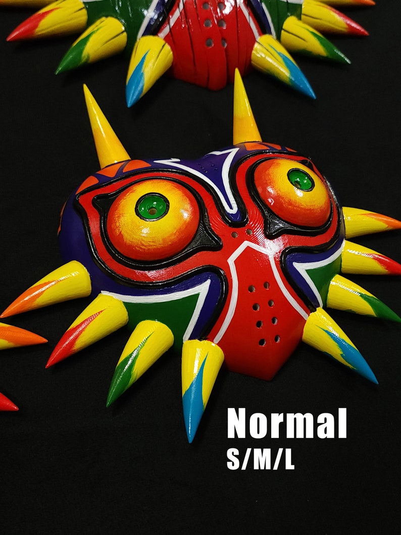 May include: A colorful Majora's Mask replica with yellow, red, green, blue, and black paint. The mask has a sharp, pointed design with spikes around the edges. The text "Normal S/M/L" is visible below the mask.