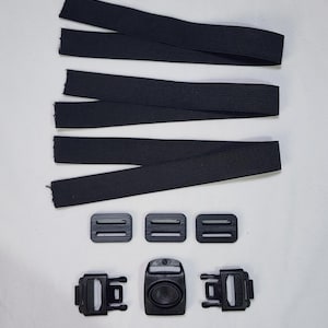 May include: Black elastic straps and plastic buckles. The image shows four black elastic straps, three small rectangular buckles, and three larger buckles with a central oval-shaped clasp. The components are arranged on a white surface.