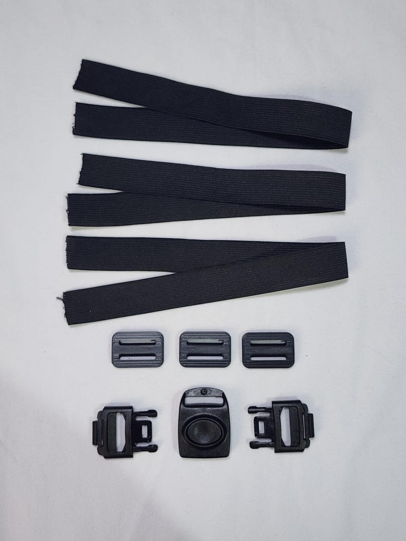 May include: Black elastic straps and plastic buckles. The image shows four black elastic straps, three small rectangular buckles, and three larger buckles with a central oval-shaped clasp. The components are arranged on a white surface.