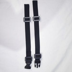 May include: Two black adjustable straps with gray plastic buckles and a black plastic clip. The straps are made of a woven material and are designed to be used with a variety of items.