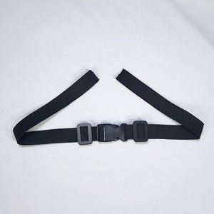 May include: A black elastic belt with a plastic buckle closure. The belt has two rectangular plastic loops and a center buckle. The elastic band is split at the ends.