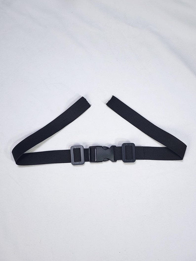 May include: A black elastic belt with a plastic buckle closure. The belt has two rectangular plastic loops and a center buckle. The elastic band is split at the ends.