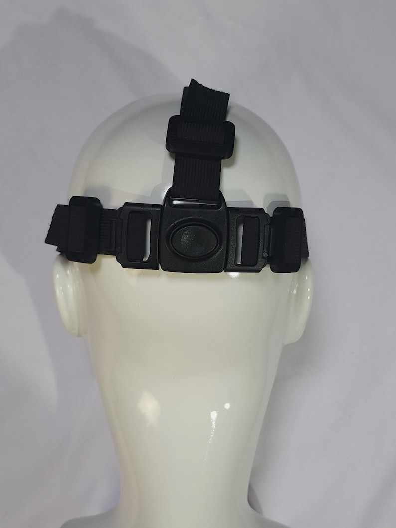 May include: Black headlamp strap with adjustable buckles and a top strap, designed to fit around the head. The strap is shown on a white mannequin head, against a white background. The strap is made of a durable, woven material.