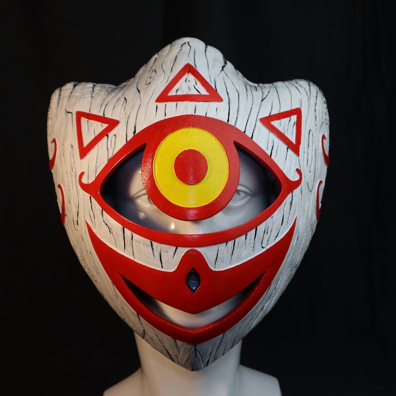 May include: A white mask with a red and yellow eye design. The mask has a wood grain texture and a red smile.
