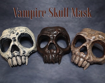 May include: Three vampire skull masks in a row. The masks are in shades of white, brown, and tan. Each mask has large eye sockets, a prominent nose cavity, and sharp, pointed teeth. The text "Vampire Skull Mask" is above the masks.