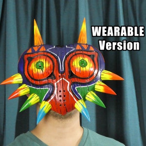 May include: A colorful, wearable Majora's Mask from The Legend of Zelda. The mask is made of wood and painted with red, orange, yellow, green, blue, and purple. It has a sharp, pointed design with spikes around the edges.