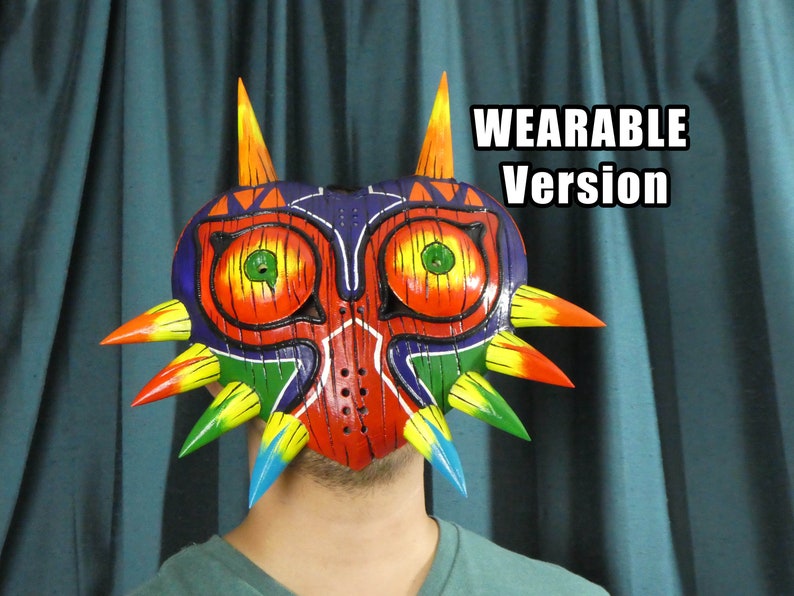 May include: A colorful, wearable Majora's Mask from The Legend of Zelda. The mask is made of wood and painted with red, orange, yellow, green, blue, and purple. It has a sharp, pointed design with spikes around the edges.