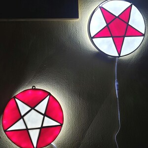May include: Two round stained glass light fixtures with a white pentagram on a red background. The lights are hanging on a wall.