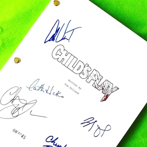May include: A white script titled "Child's Play" with multiple signatures in blue and black ink. The title is in a bold, outlined font with a blood-red slash through the "A". The script is dated October 20, 1987, and has gold binding posts.