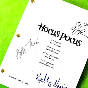 May include: A white Hocus Pocus screenplay with signatures and the date Wednesday, May 13, 1992. The title is in a stylized font. The document has three gold-colored fasteners and is on a bright green background.