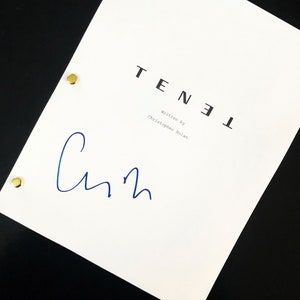 May include: A white script with the title "TENET" printed in black, with the words "Written by Christopher Nolan" below. A blue signature is present. The script is held together with three gold brads.