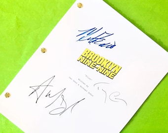 May include: A white script with the title "Brooklyn Nine-Nine" and the word "Pilot" printed on it. The script has multiple signatures in blue and black ink. The background is a bright green.
