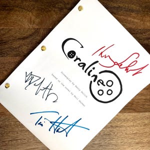 May include: A white sheet of paper with the title "Coraline" in black script and a button graphic. The screenplay is based on the novel by Neil Gaiman. Several signatures in black, red, and blue ink are visible.
