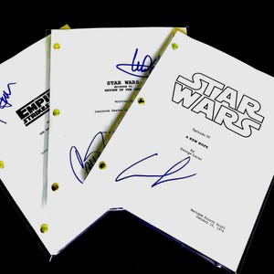 May include: Three Star Wars movie scripts, each with a different title and signatures in blue ink. The scripts are white with black text and yellow binding posts. The titles include "The Empire Strikes Back" and "A New Hope".