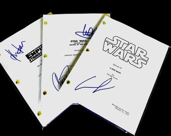 May include: Three Star Wars movie scripts, each with a different title and signatures in blue ink. The scripts are white with black text and yellow binding posts. The titles include "The Empire Strikes Back" and "A New Hope".