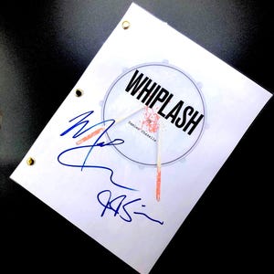 May include: A white sheet of paper with the title "WHIPLASH" in bold black letters, featuring a drum graphic. The paper has blue signatures and gold eyelets. The text "by Damien Chazelle" is also visible.
