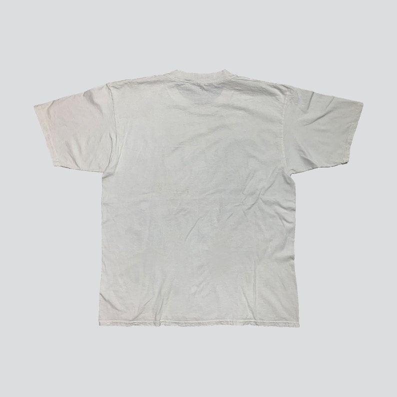 May include: A plain white t-shirt, viewed from the back, with a crew neck and short sleeves. The shirt is made of a soft, slightly wrinkled fabric. The background is a solid light gray.