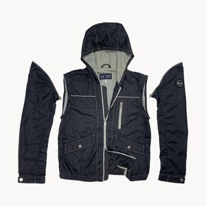 May include: Black hooded vest with detachable sleeves. The vest has a gray interior, a zipper closure, and two front pockets. The sleeves are also black and have a button closure at the wrist. The vest has the text "AJ Armani Jeans" on the label.