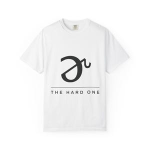May include: A white short-sleeved t-shirt featuring a black graphic of the schwa symbol above a horizontal line and the text THE HARD ONE in black capital letters centred on the chest area of the garment.
