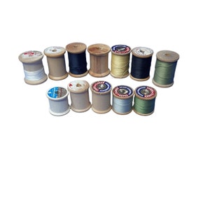 May include: A collection of 12 wooden spools of thread in various colors, including white, black, green, and beige. The spools are all the same size and shape, and they are arranged in a row.