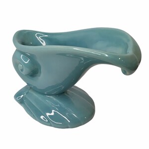 May include: A light blue ceramic serving dish shaped like a bird with a curved spout. The dish has a smooth, glossy finish.