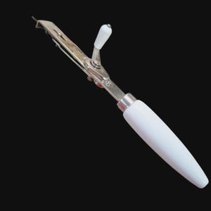 May include: A vintage can opener with a white wooden handle and a silver-colored metal body. The can opener has a crank and a blade for opening cans. The handle is smooth and tapered, and the metal components are shiny.