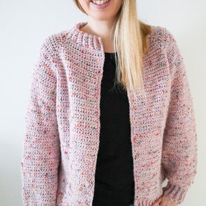 May include: A pink crocheted cardigan with colourful flecks throughout. The cardigan has a simple, open front design and long sleeves.