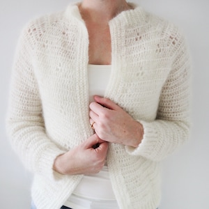 May include: A white crocheted cardigan with a open front and long sleeves.