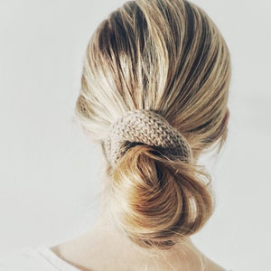 May include: A woman with long, light blonde hair is wearing a brown knitted hair scrunchie to hold her hair in a bun.