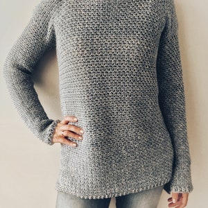 May include: A gray knitted sweater with a loose fit and long sleeves.