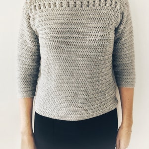 Peut inclure: Un pull en crochet gris avec un col bateau et des manches trois-quarts.