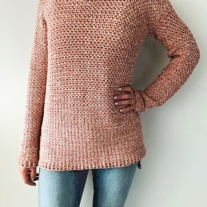 May include: A loose-fitting, long-sleeved sweater in a pink and white speckled yarn. The sweater has a round neckline and a slightly longer hem in the back.
