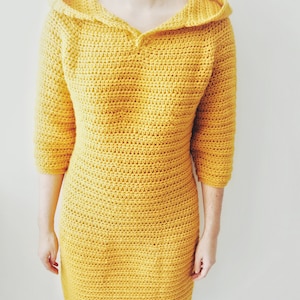 May include: A yellow crocheted dress with a hood and a v-neck.