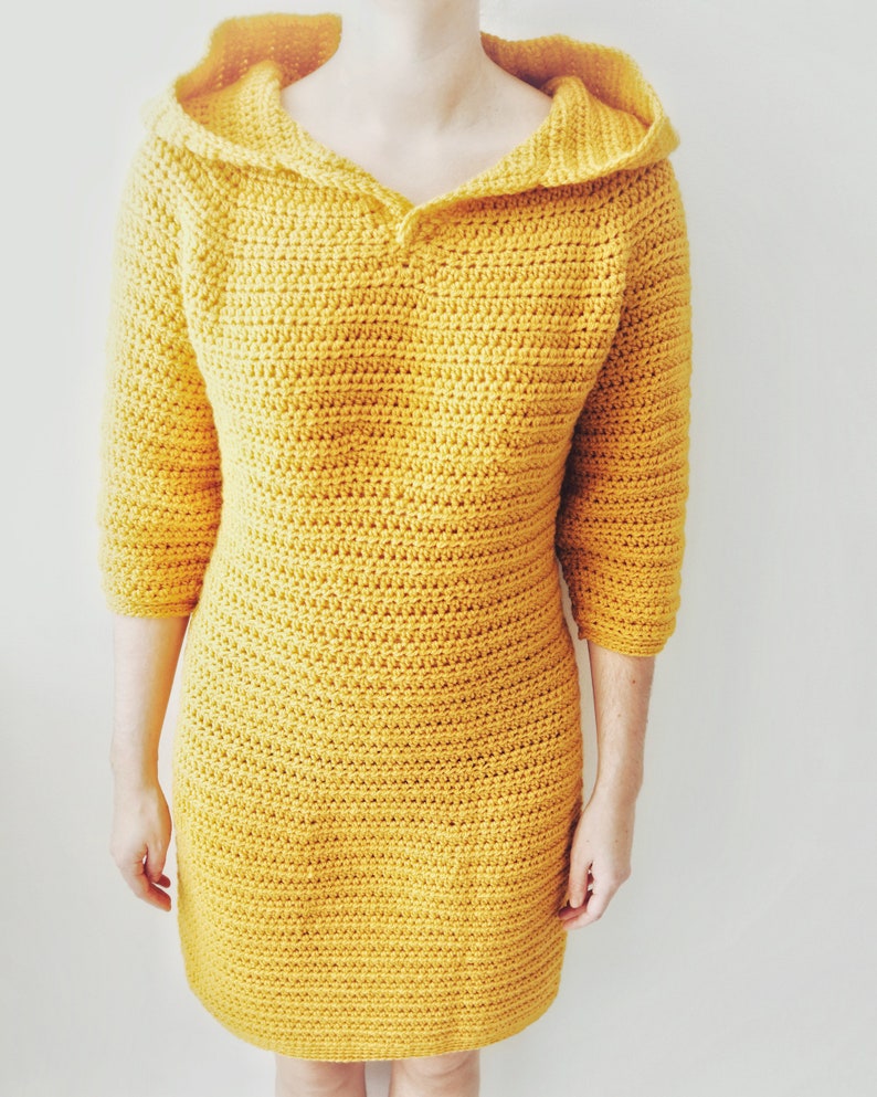 May include: A yellow crocheted dress with a hood and a v-neck.