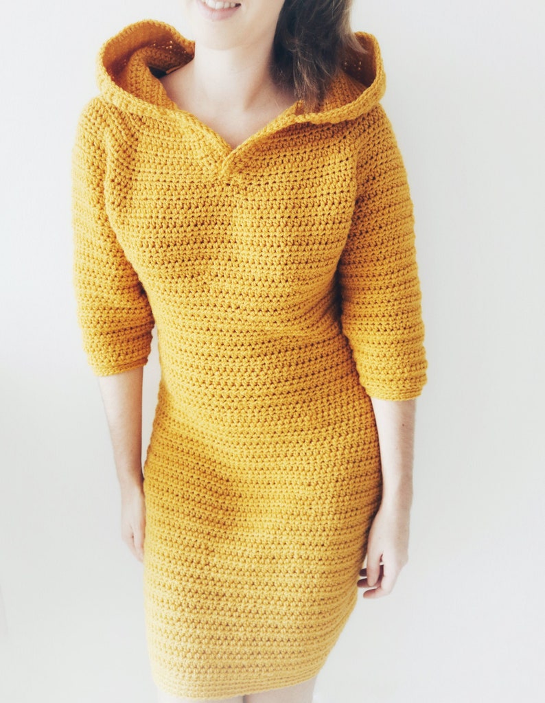 May include: A mustard yellow crocheted dress with a hood. The dress has a V-neck and three-quarter sleeves.