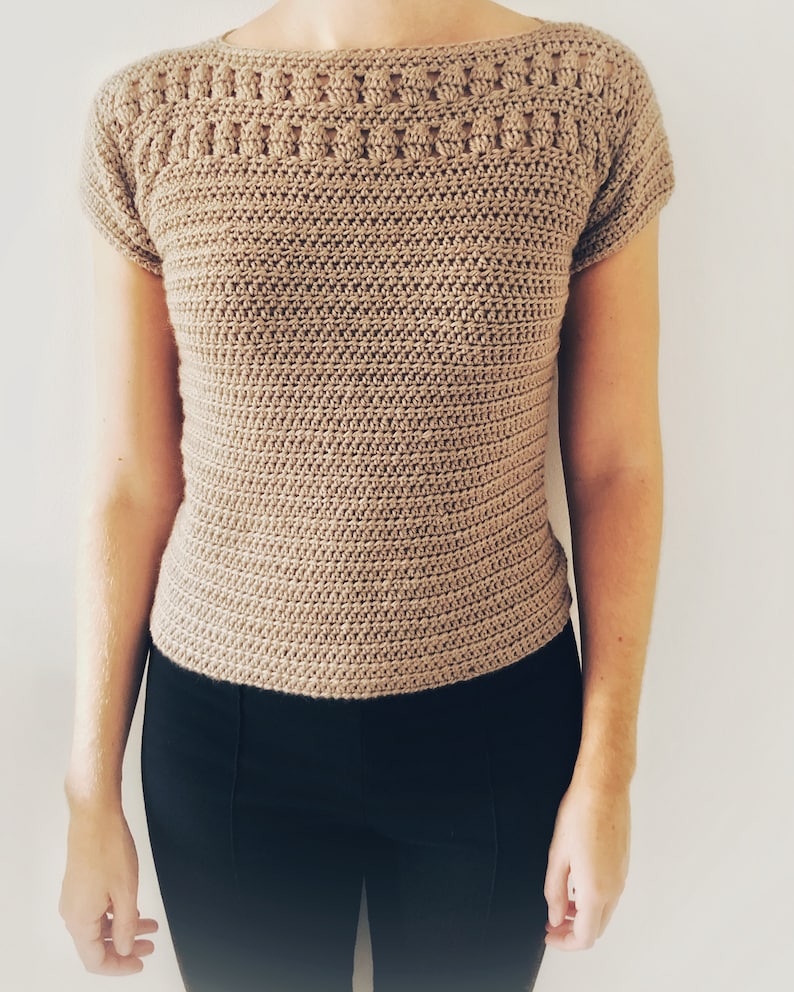 Peut inclure: Un haut crochet&eacute; &agrave; manches courtes de couleur marron. Le haut pr&eacute;sente un motif de point d&eacute;coratif autour de l'encolure.