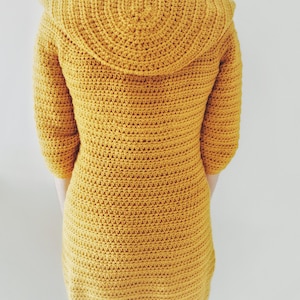 May include: A mustard yellow crocheted cardigan with a large, rounded collar. The cardigan is made with a single crochet stitch and has a fitted silhouette.