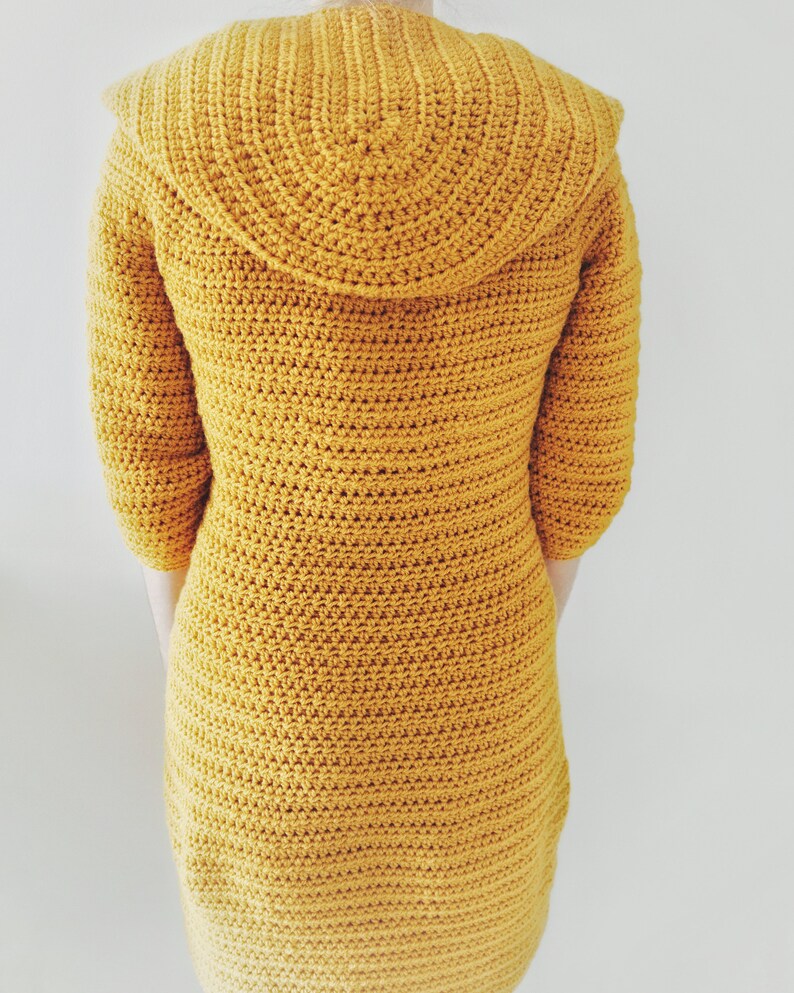 May include: A mustard yellow crocheted cardigan with a large, rounded collar. The cardigan is made with a single crochet stitch and has a fitted silhouette.