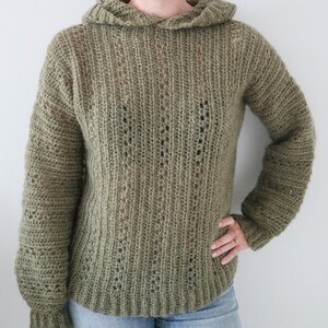 May include: A green crocheted hooded sweater with a loose fit and long sleeves.
