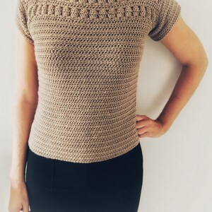 Peut inclure: Un haut en crochet beige &agrave; manches courtes et un motif de point carr&eacute;. Le haut a un col bateau et est ajust&eacute;.