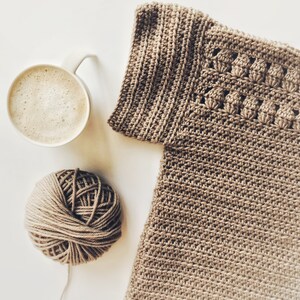 Peut inclure: Une pelote de laine brune, une tasse de caf&eacute; et un v&ecirc;tement crochet&eacute; de couleur brun clair.