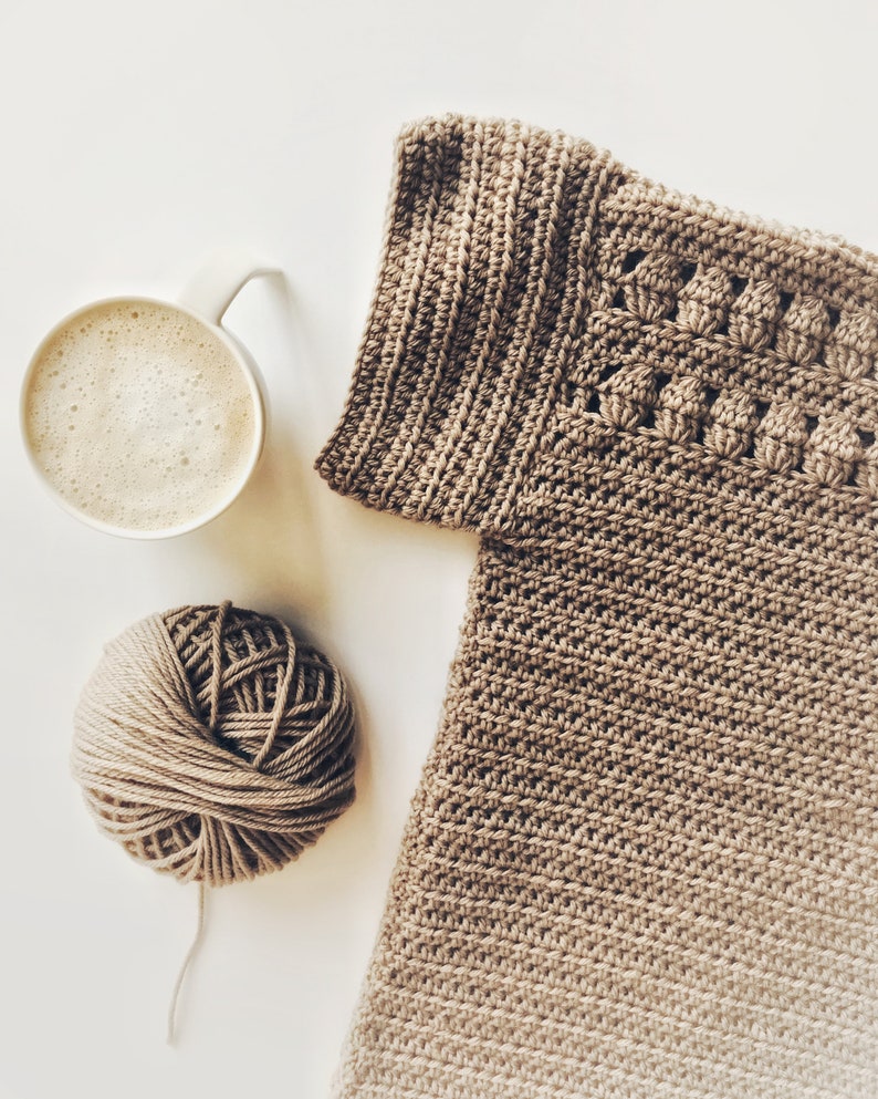Peut inclure: Une pelote de laine brune, une tasse de caf&eacute; et un v&ecirc;tement crochet&eacute; de couleur brun clair.